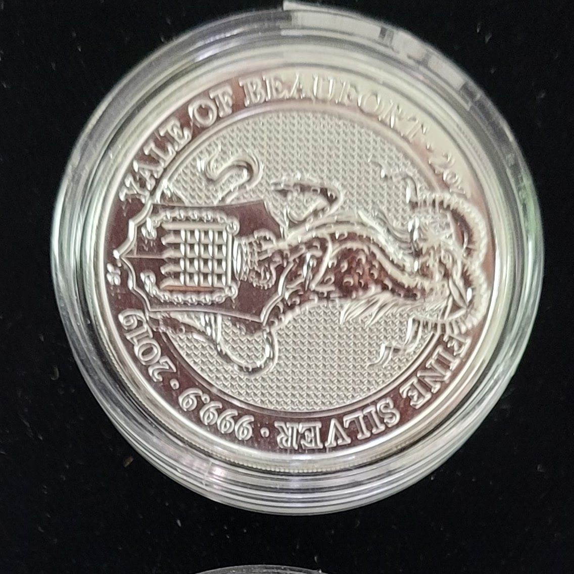 Silver coin in a plastic case with a design of a mythical creature and text 