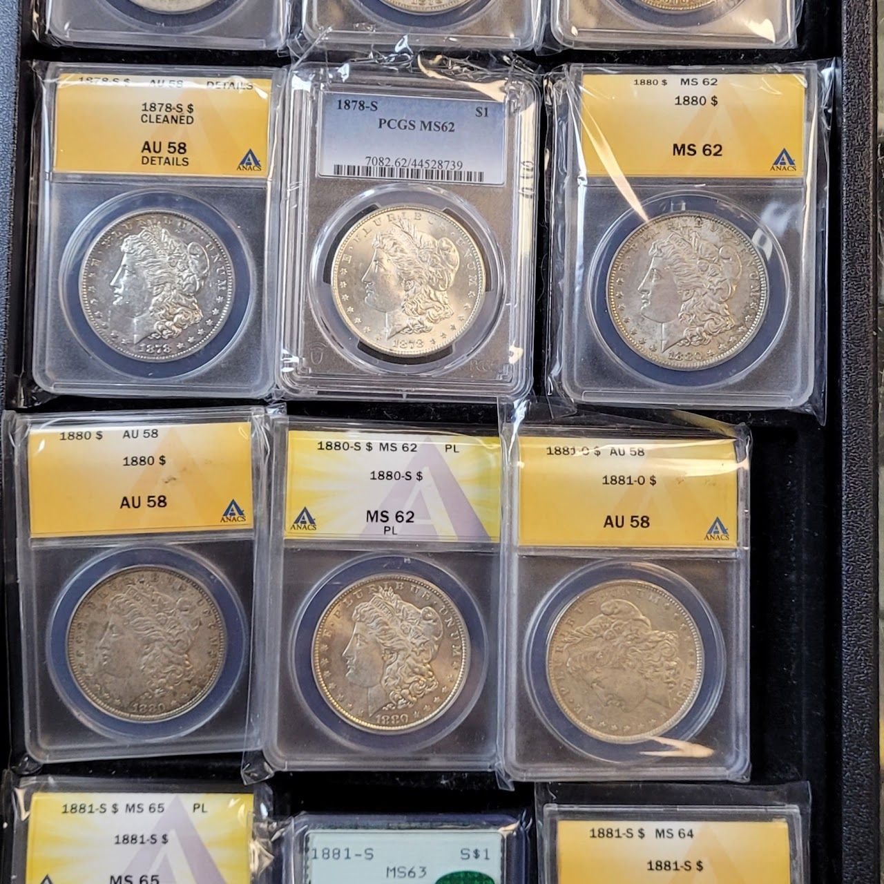 Rows of graded silver coins in plastic holders. Labels indicate grade, with varying conditions like AU, MS, and grades from PCGS.