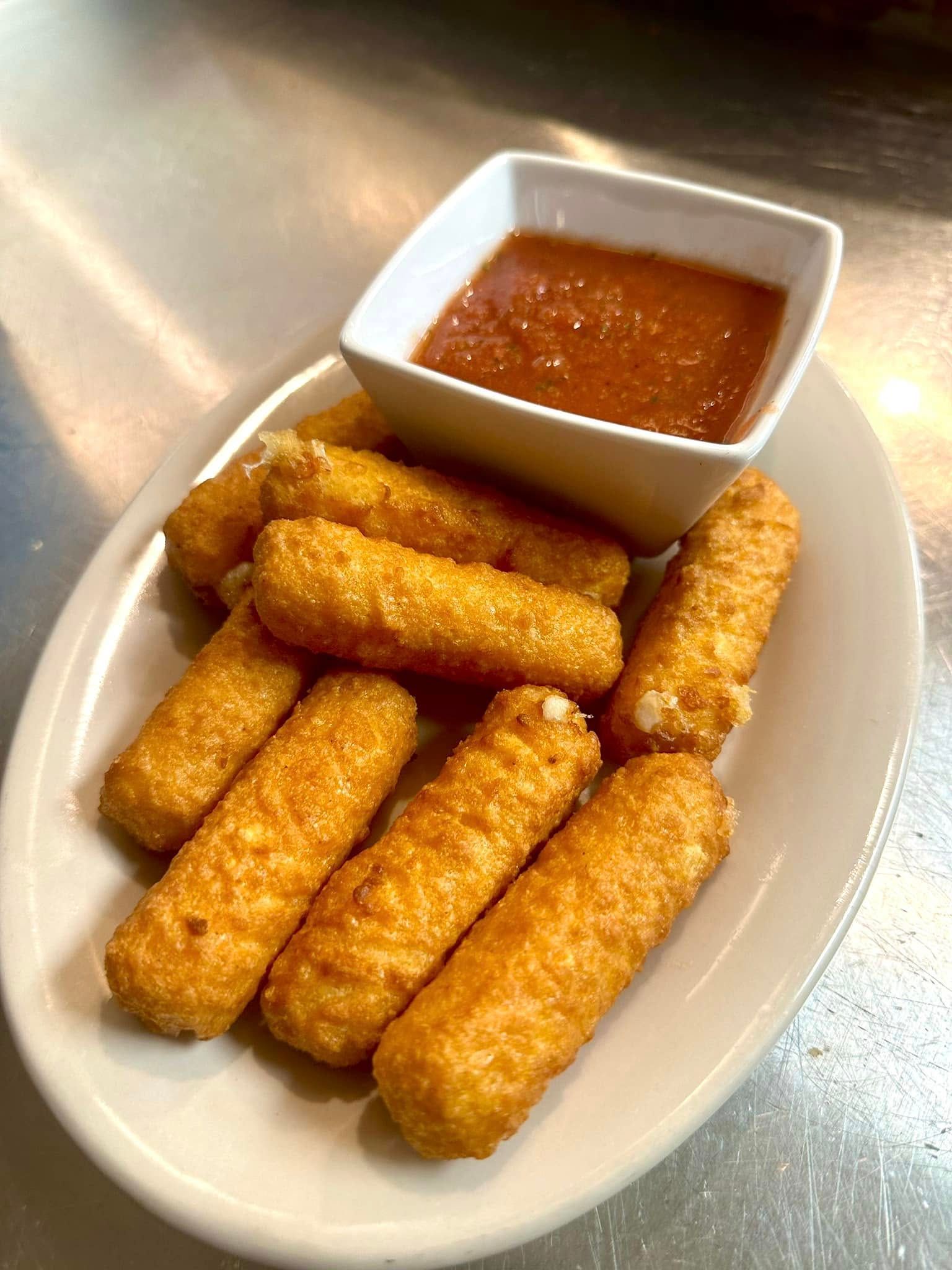 A plate of mozzarella sticks with dipping sauce on a table.