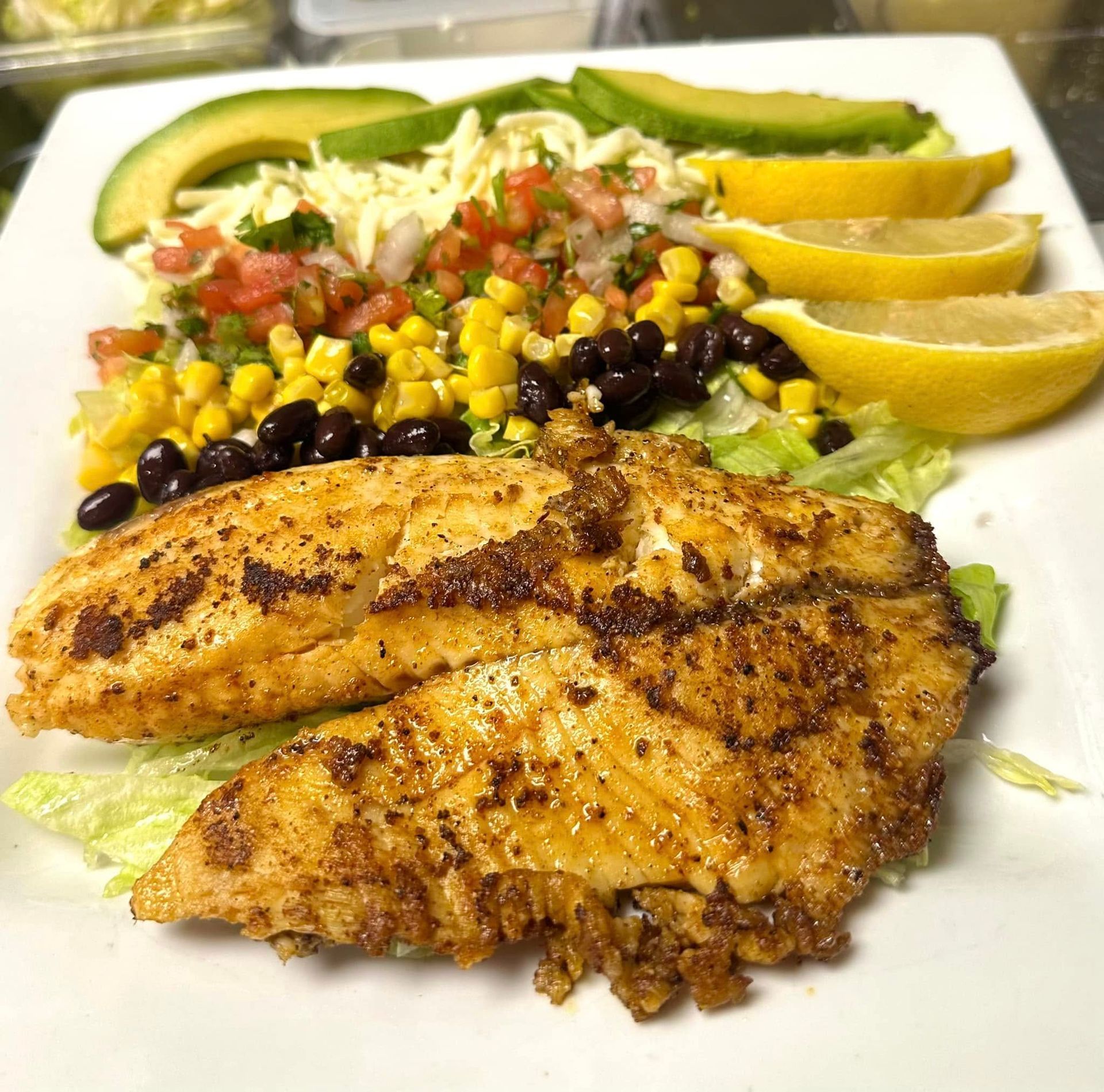 A white plate topped with chicken , avocado , corn , black beans and salsa.