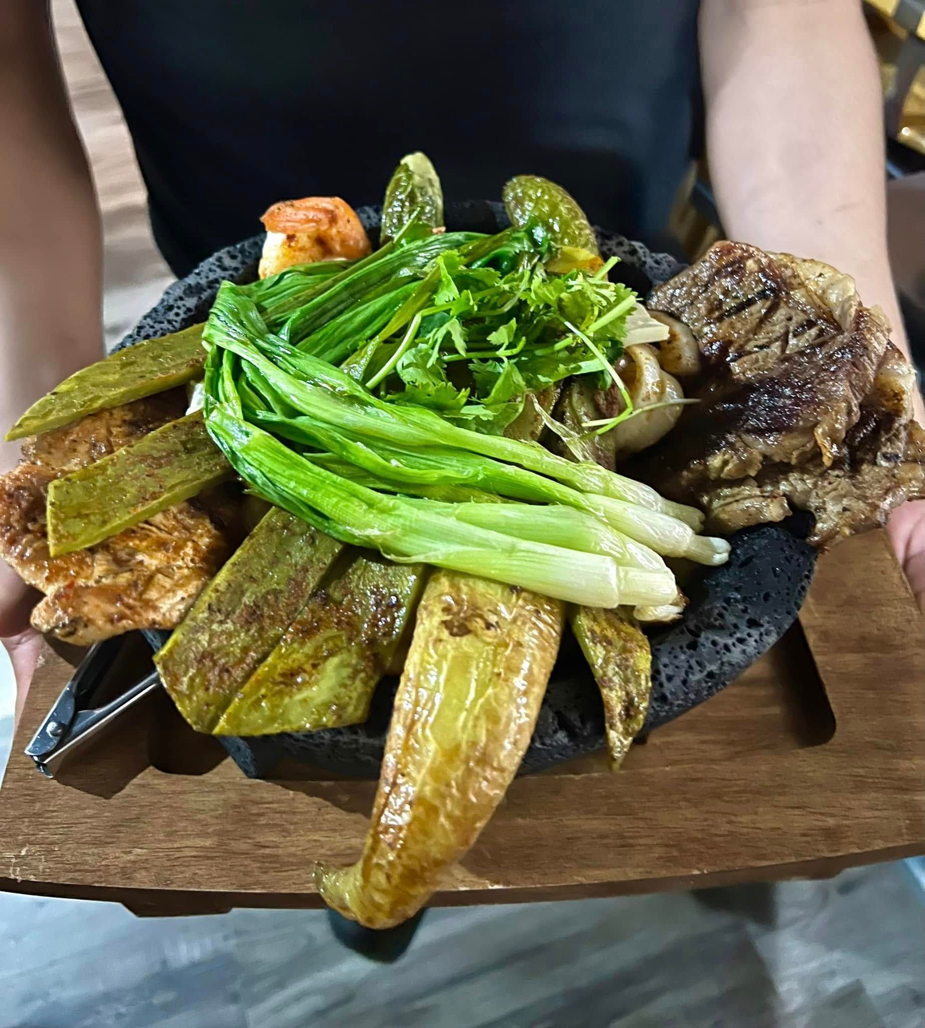 A person is holding a plate of food on a wooden tray.