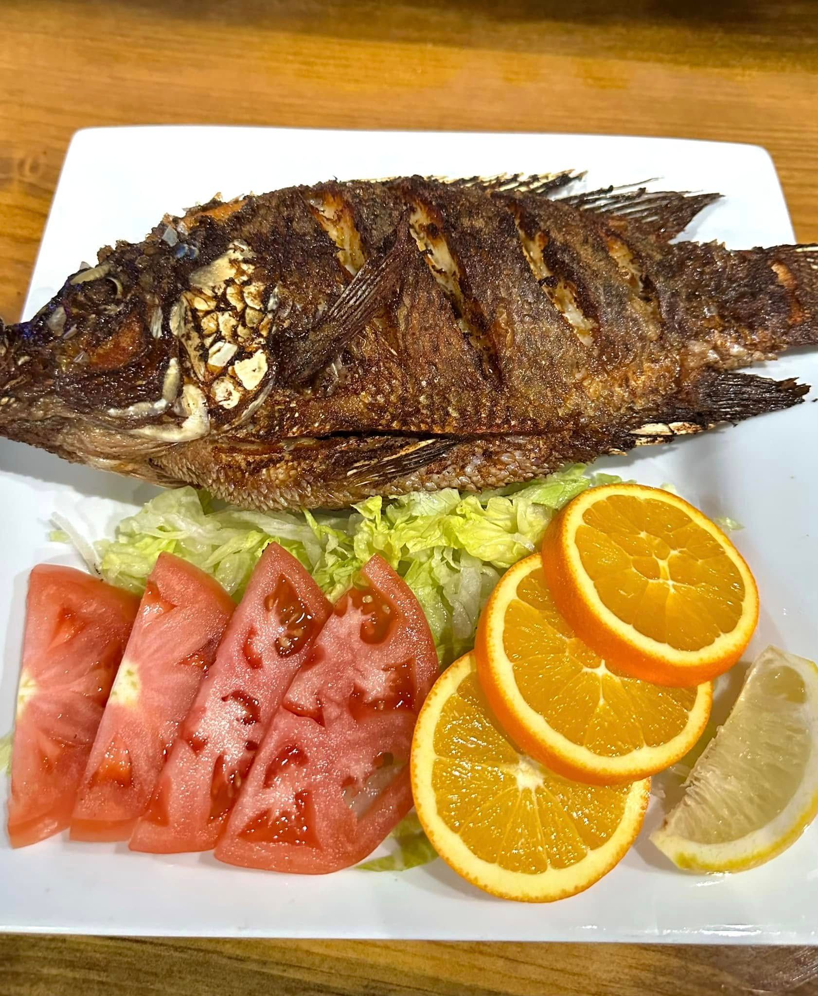 A white plate topped with a fish , tomatoes , oranges and lemon slices.