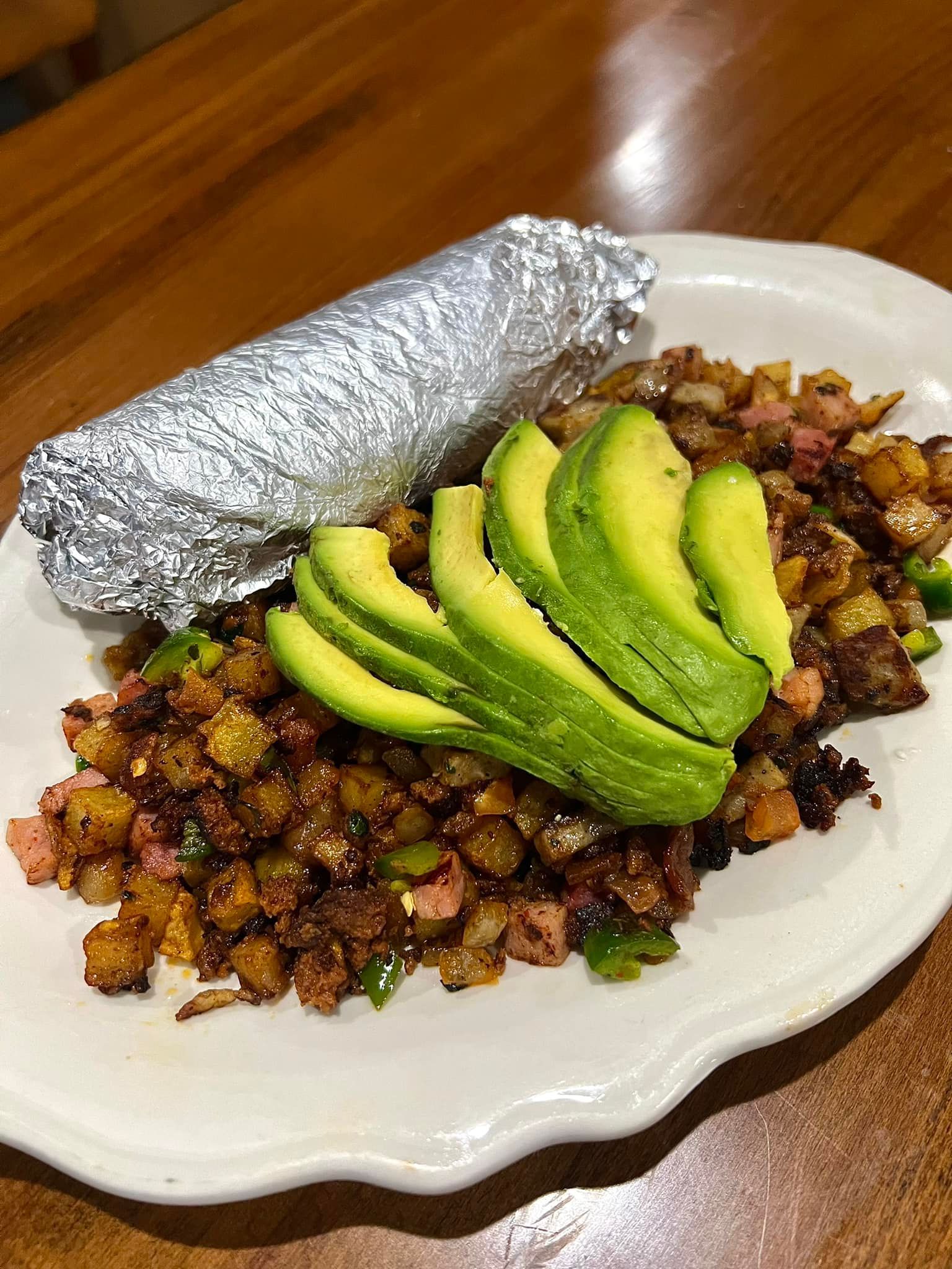 A plate of food with avocado and a baked potato on a table.