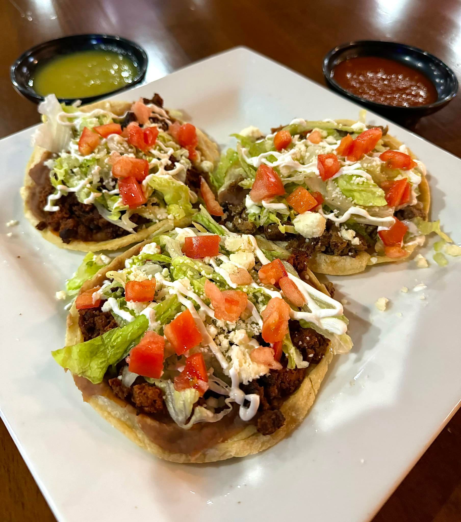 A white plate topped with three tacos with tomatoes , lettuce , and sour cream.