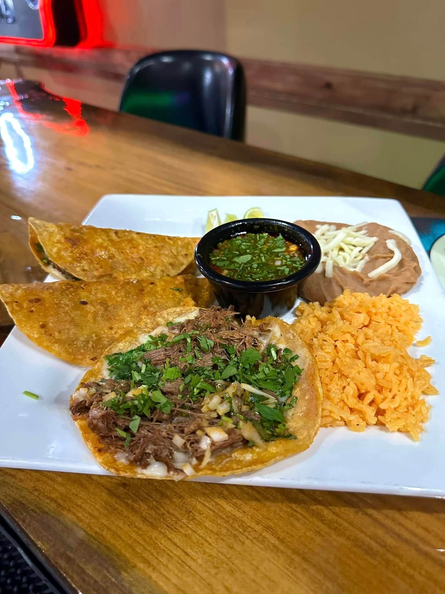 A white plate topped with tacos , rice and beans on a wooden table.