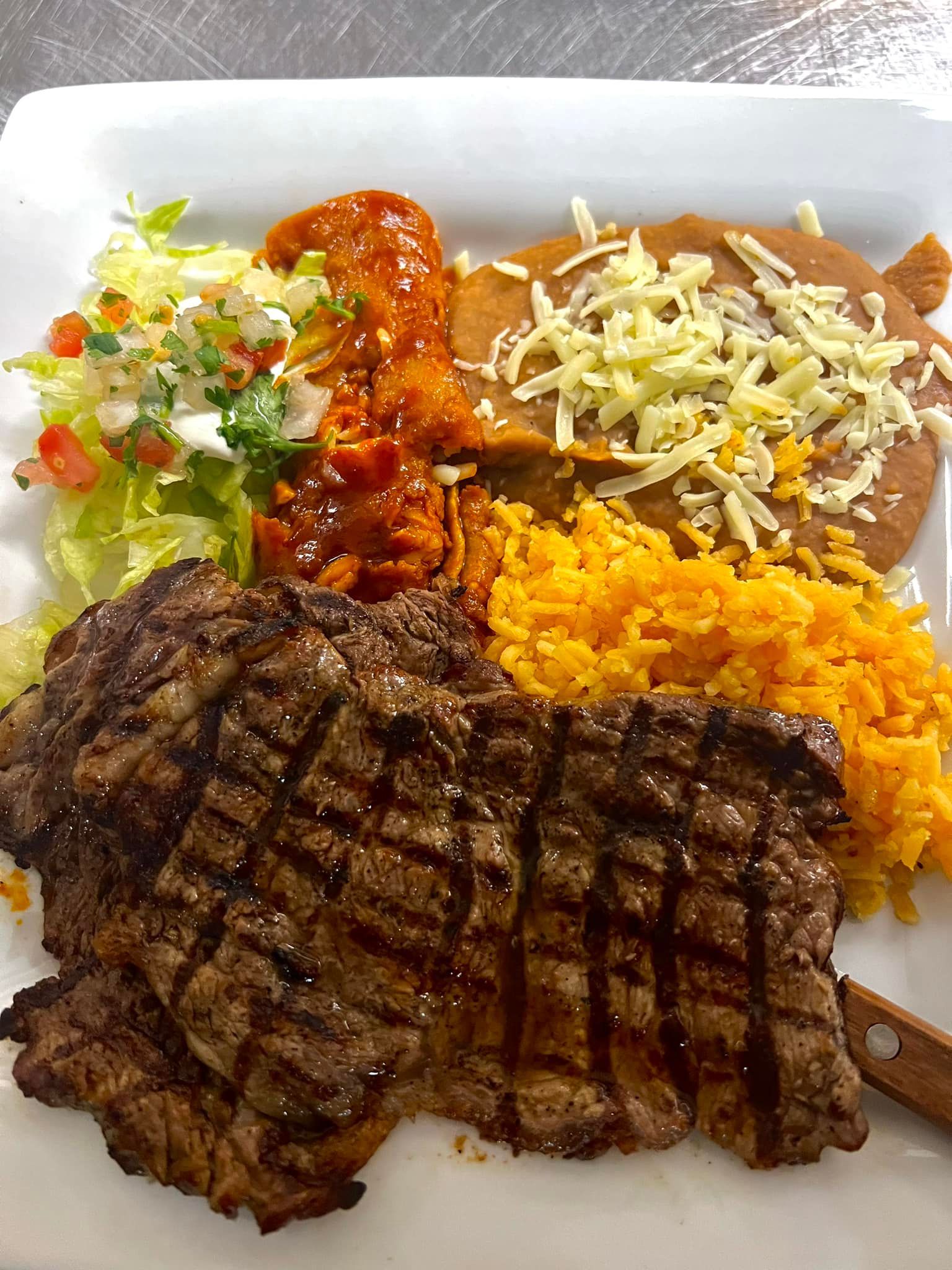 A white plate topped with a steak , rice , and beans.