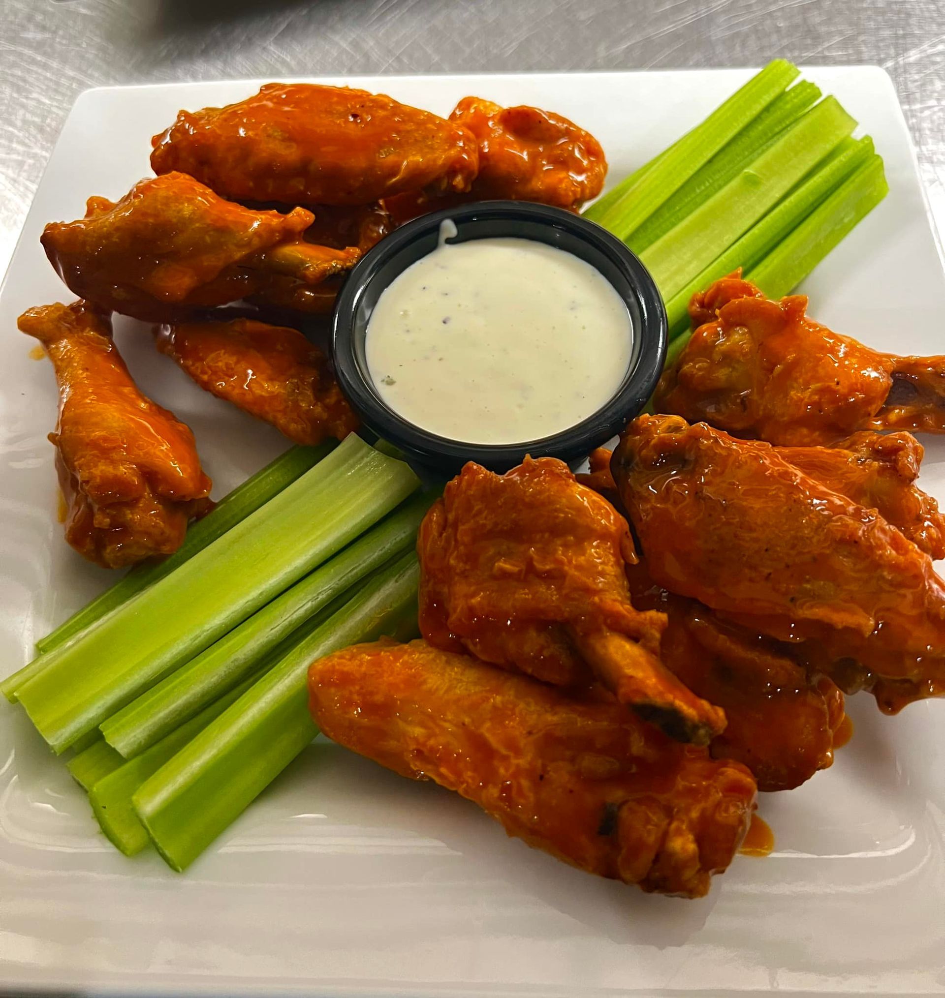 A white plate topped with chicken wings celery and ranch dressing