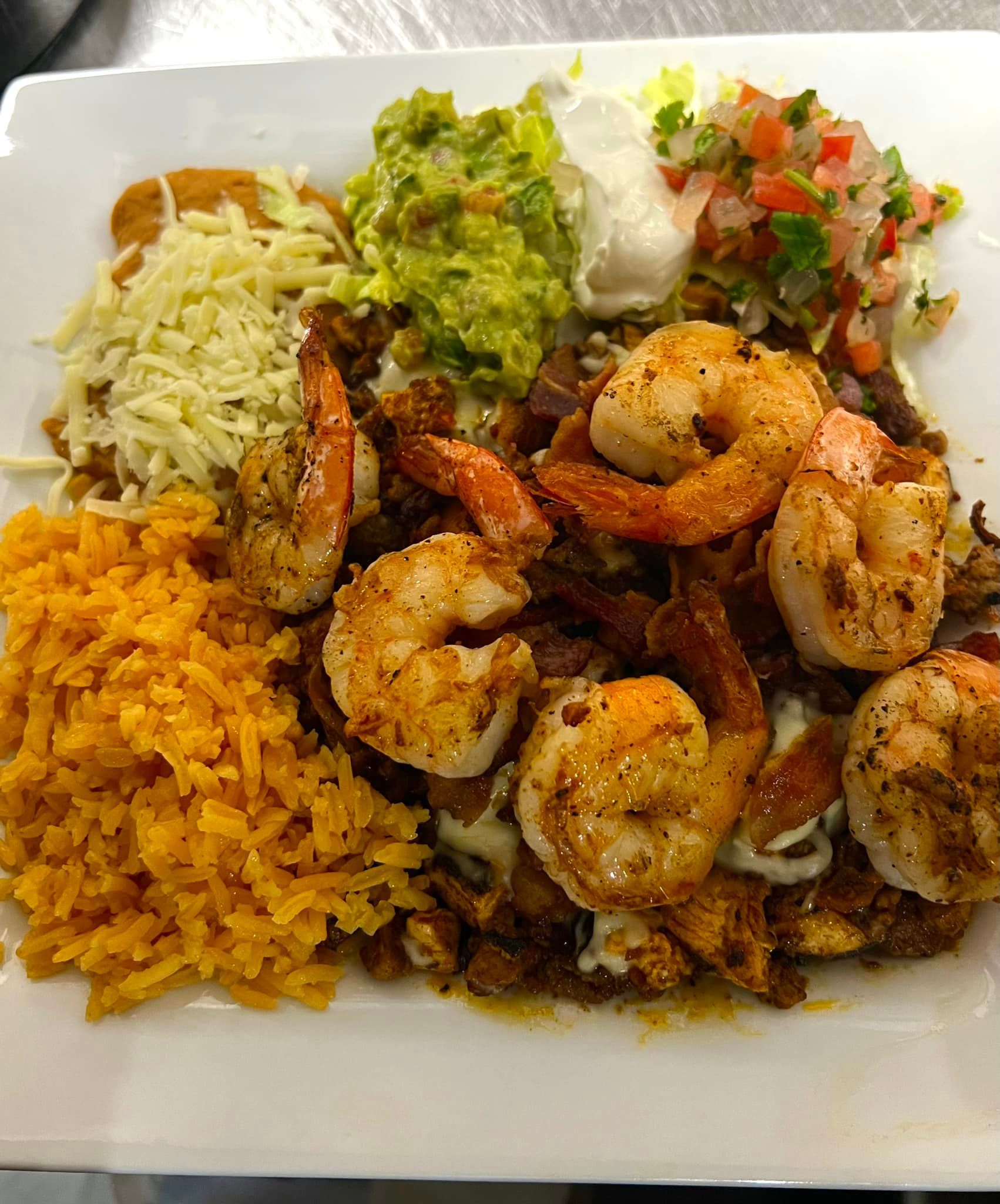 A white plate topped with shrimp , rice , guacamole and cheese.