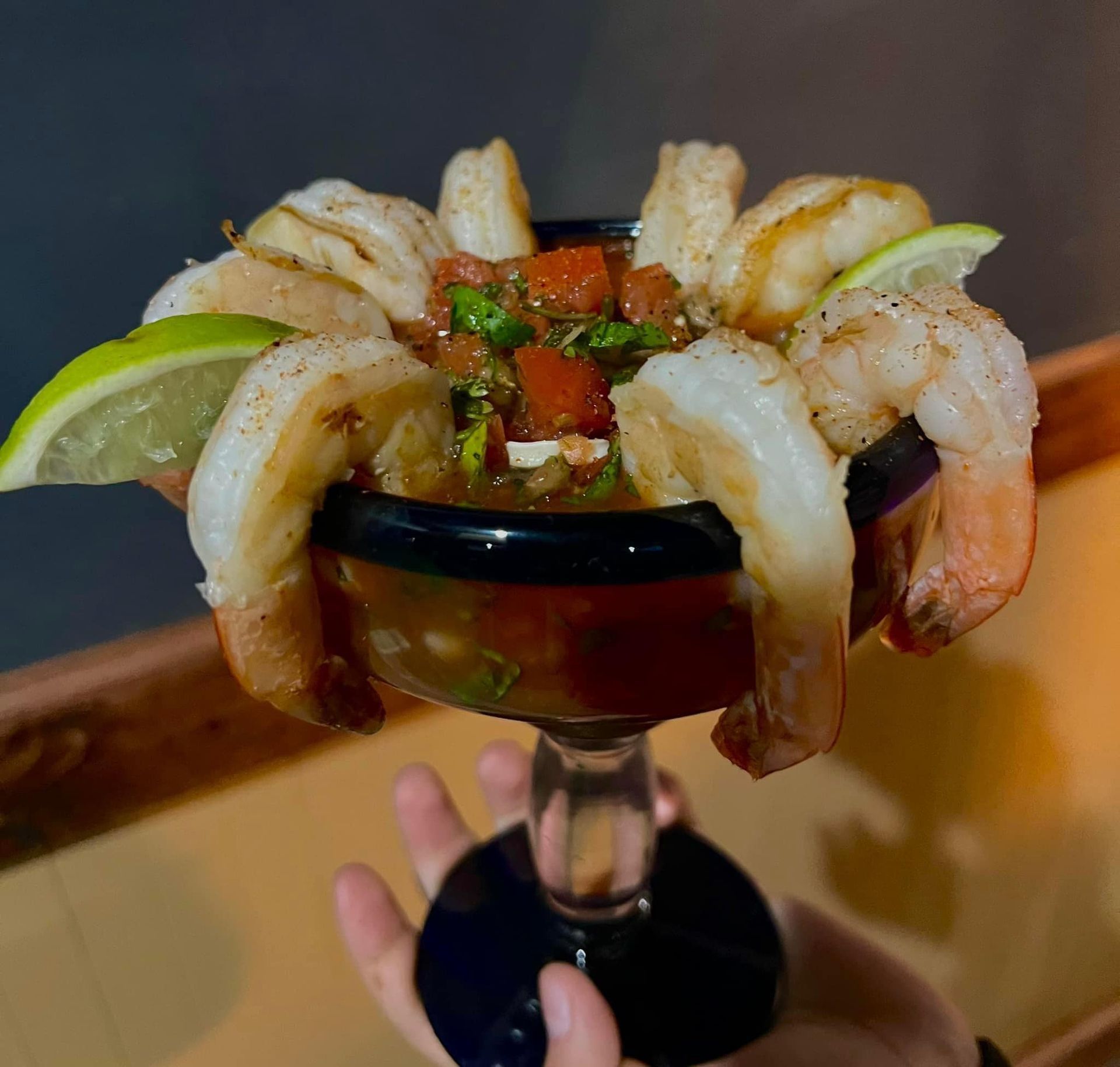 A person is holding a martini glass filled with shrimp and vegetables.