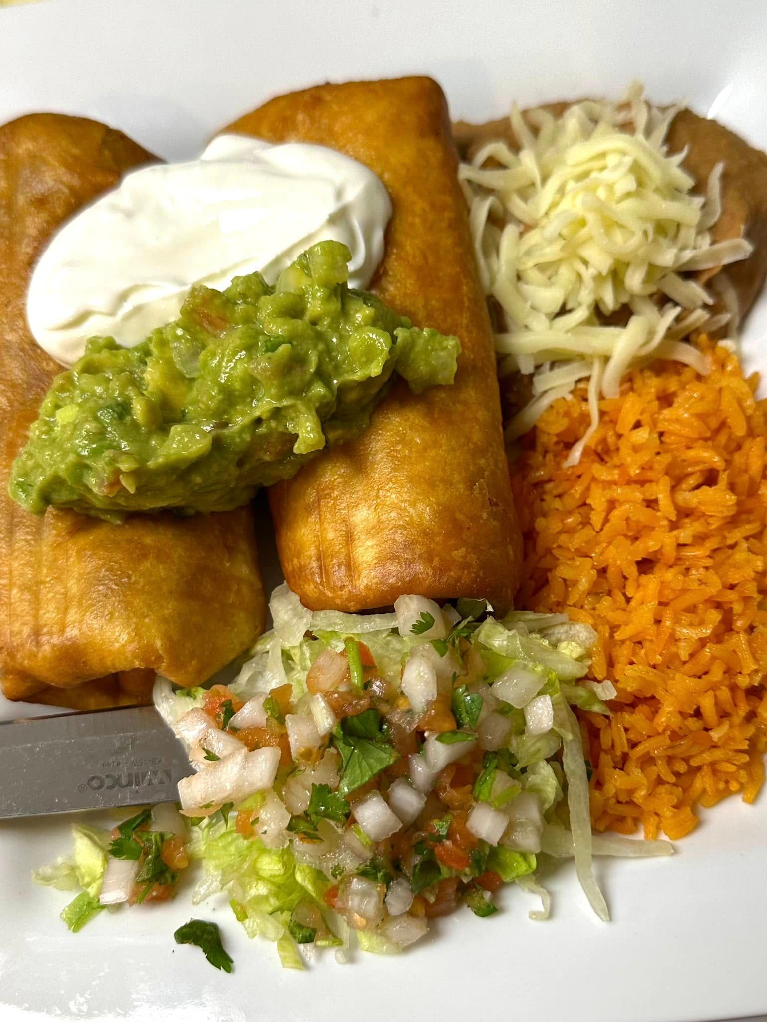 A white plate topped with burritos , guacamole , rice and beans.
