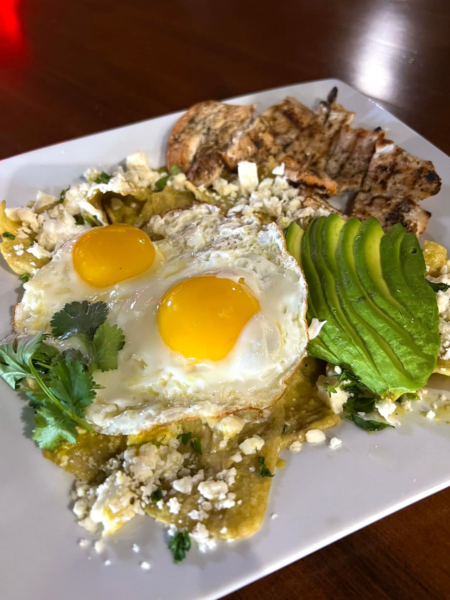 A plate of food with eggs , avocado and chicken on a table.