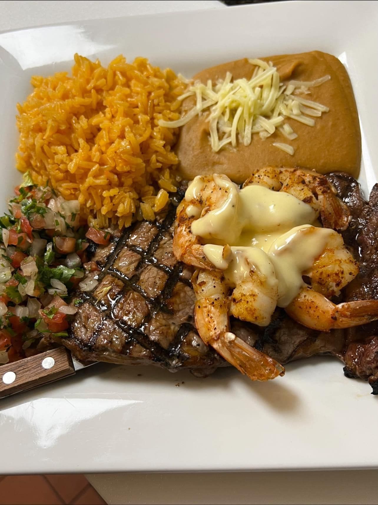 A white plate topped with a steak , shrimp , rice and beans.