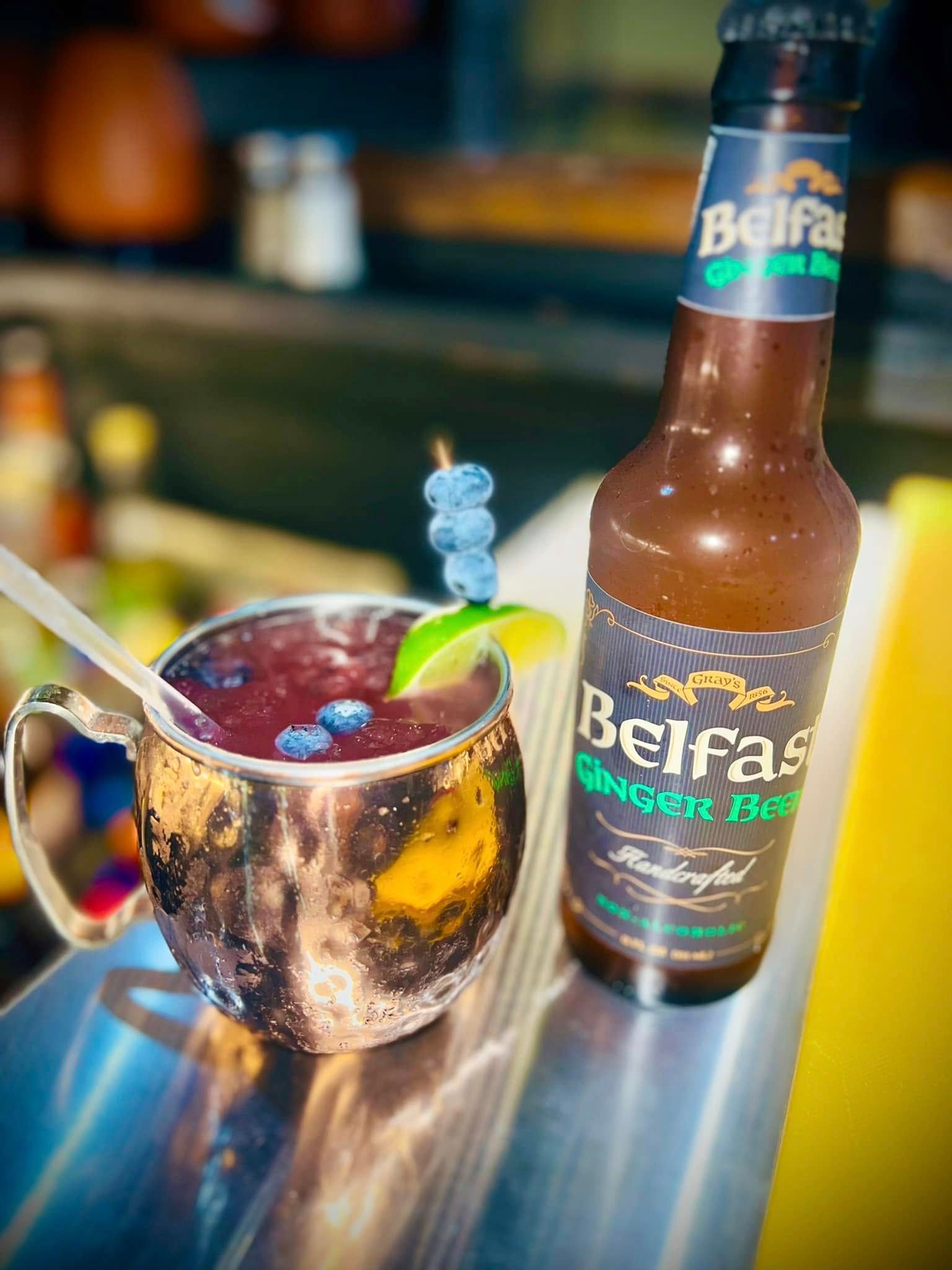 A bottle of belfast ginger beer is next to a cup of drink.