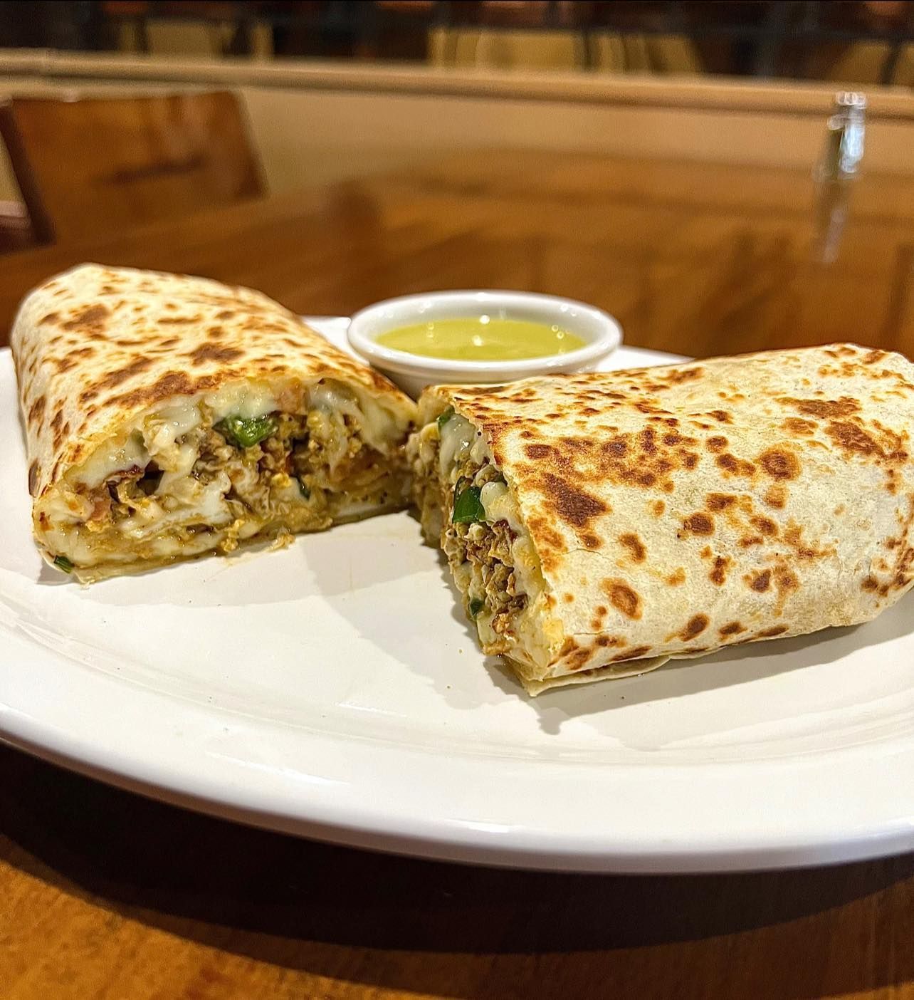 Two burritos are on a white plate with a dipping sauce.