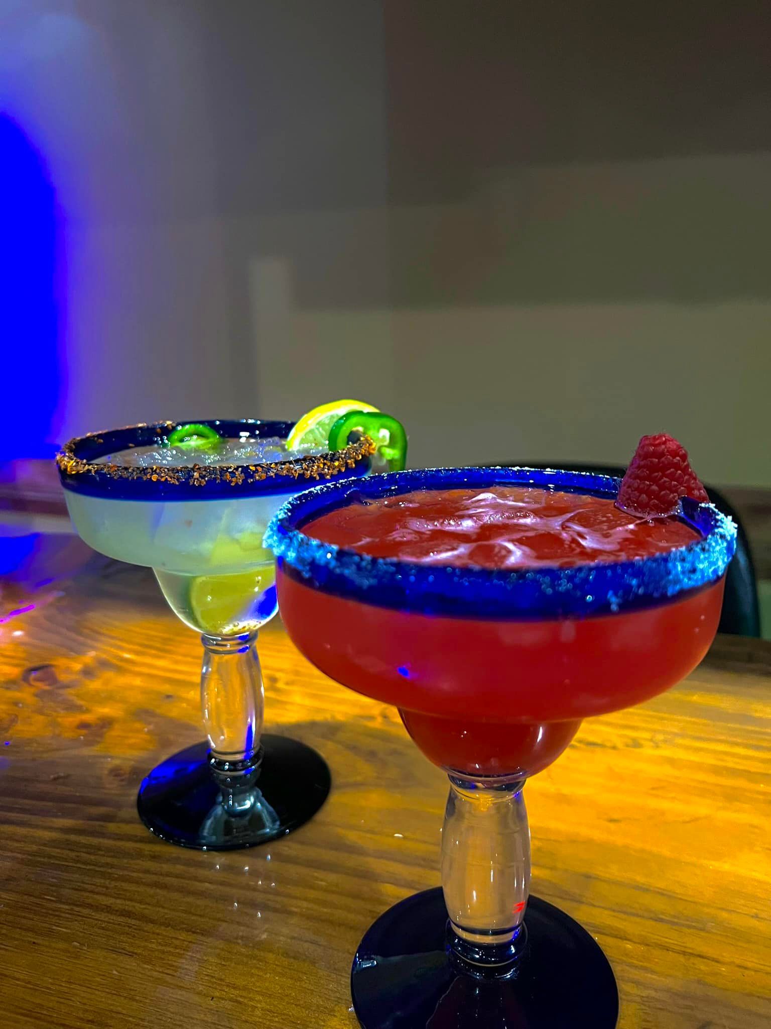 Two margaritas are sitting on a wooden table.