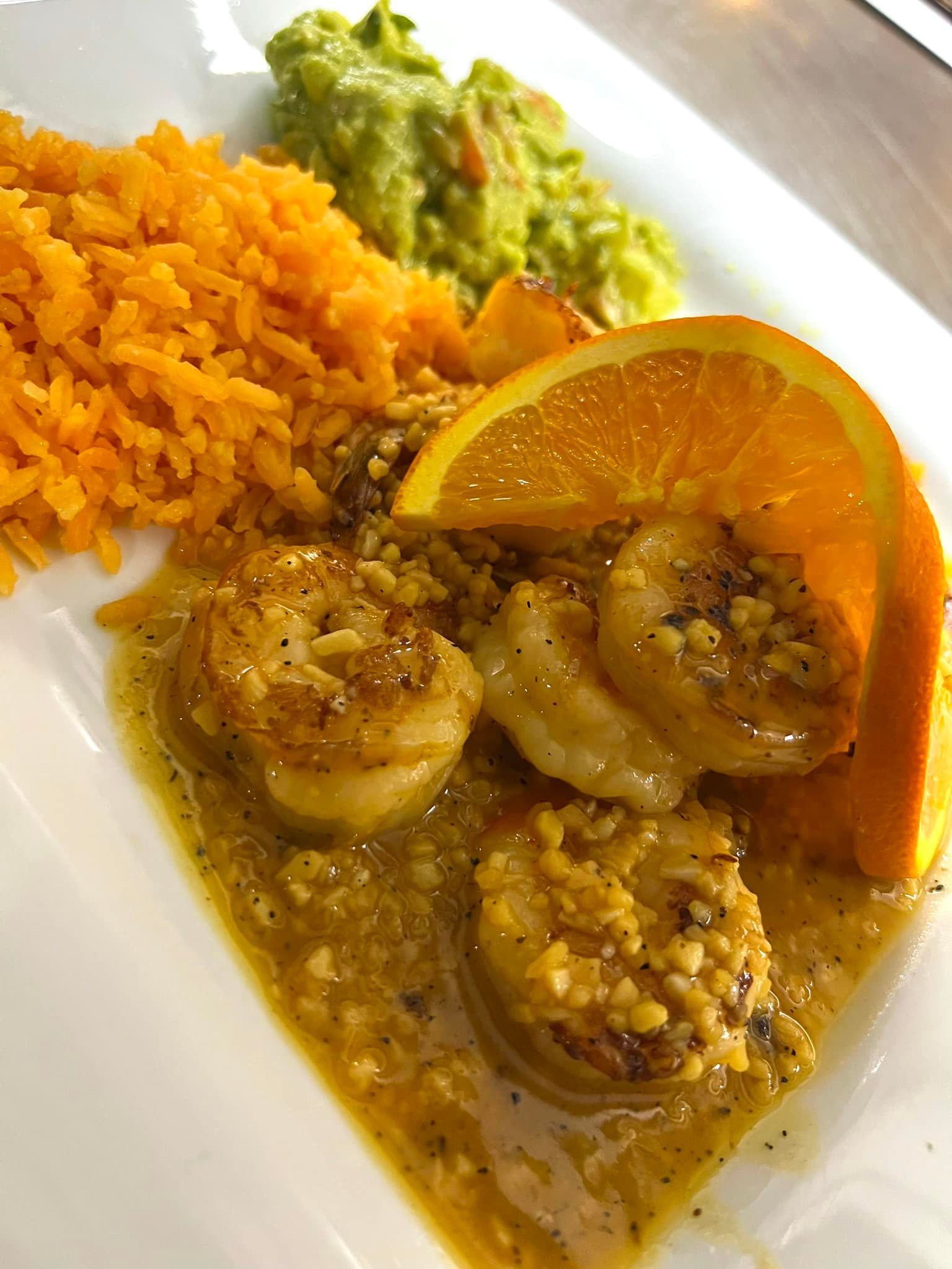 A white plate topped with shrimp , rice , guacamole and an orange slice.