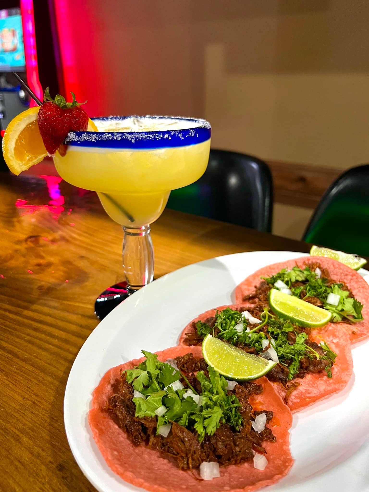 A plate of tacos and a margarita on a table.