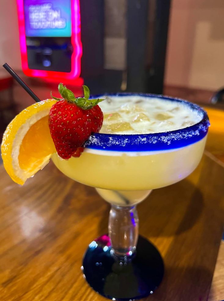 A margarita with a strawberry and a lemon slice on a wooden table.