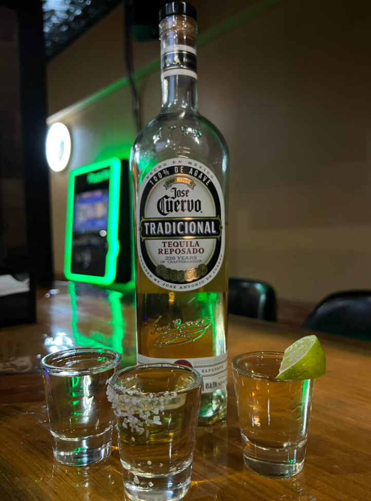 A bottle of tequila and three shot glasses on a table.