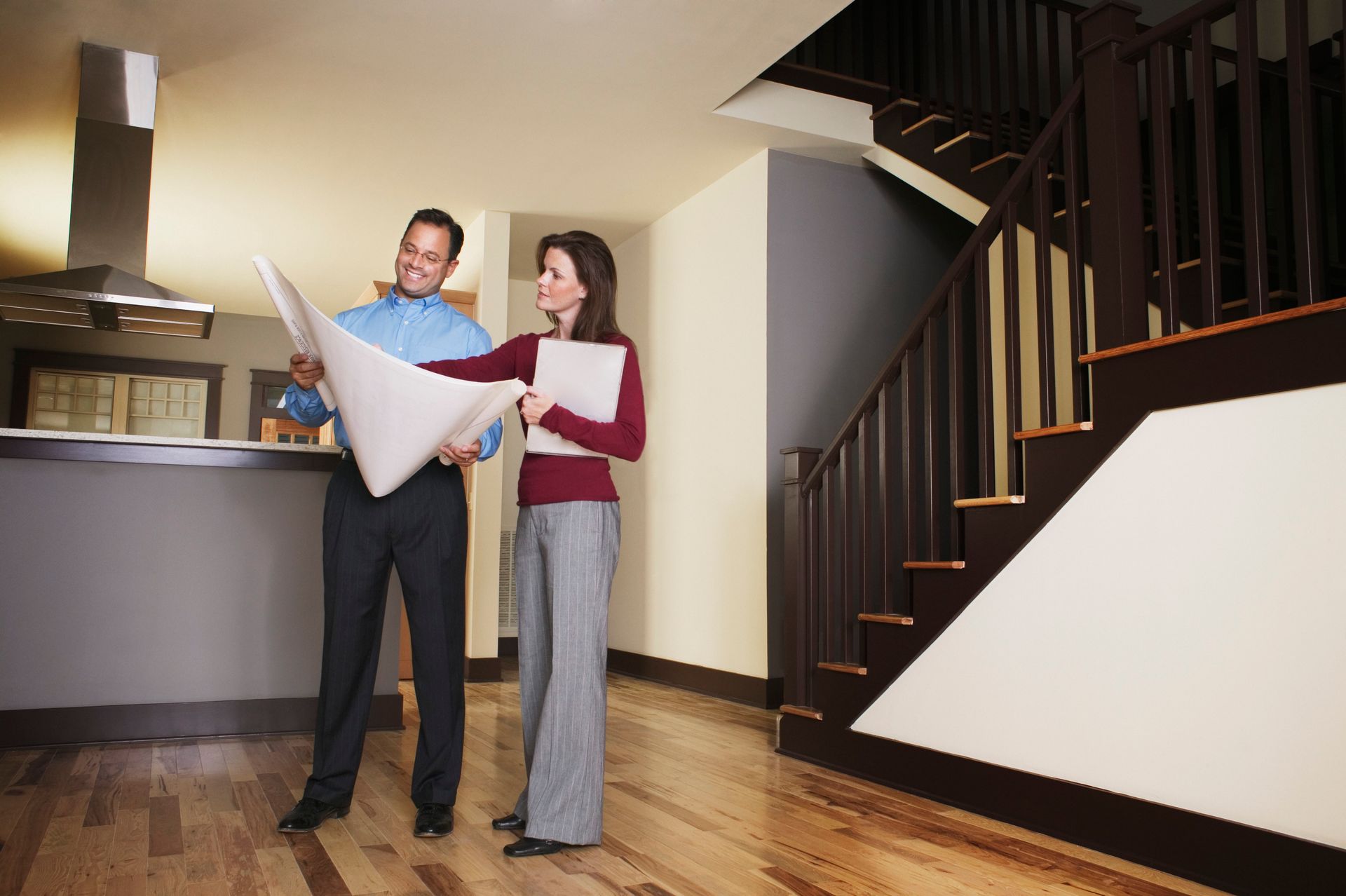 Two people reviewing architectural plans in a house with a staircase, discussing details.