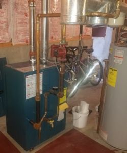 A blue furnace with copper pipes, connected to a metal chimney. A water heater is to the right. A bicycle is in the background.