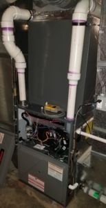 A natural gas furnace with PVC pipes extending upward; gray metal cabinet; various wires and components visible.
