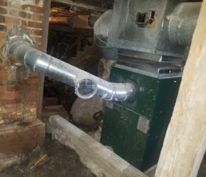 Green furnace in a basement with metal ductwork and exposed brick wall.