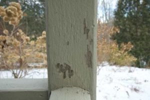 Close-up of a weathered, painted wooden post with flaking paint and snow in the background.