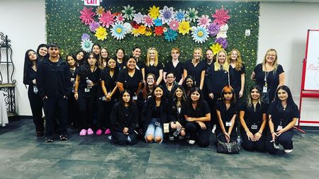 A group of people are posing for a picture in front of a wall of flowers.