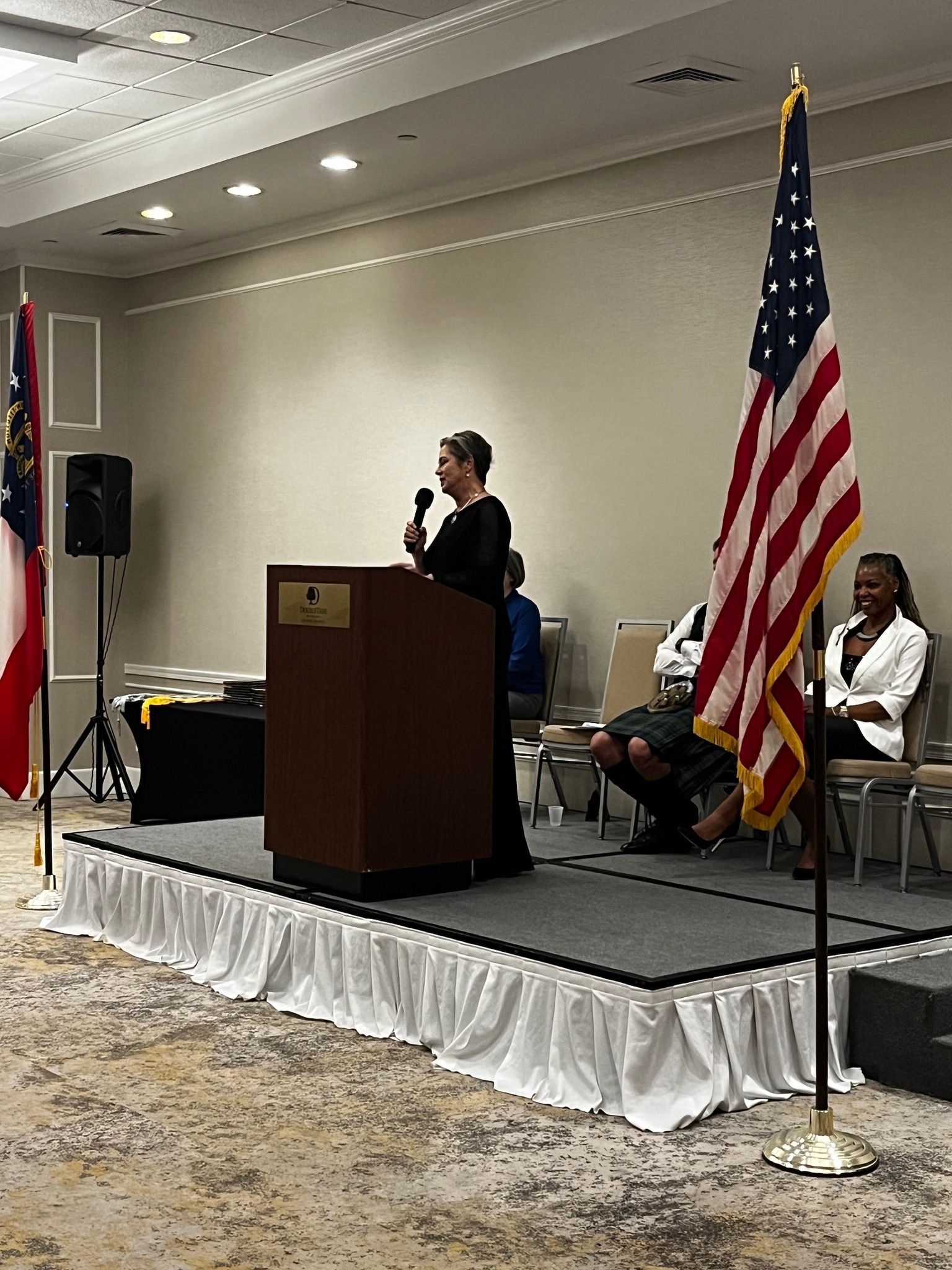 A woman is standing at a podium speaking into a microphone.