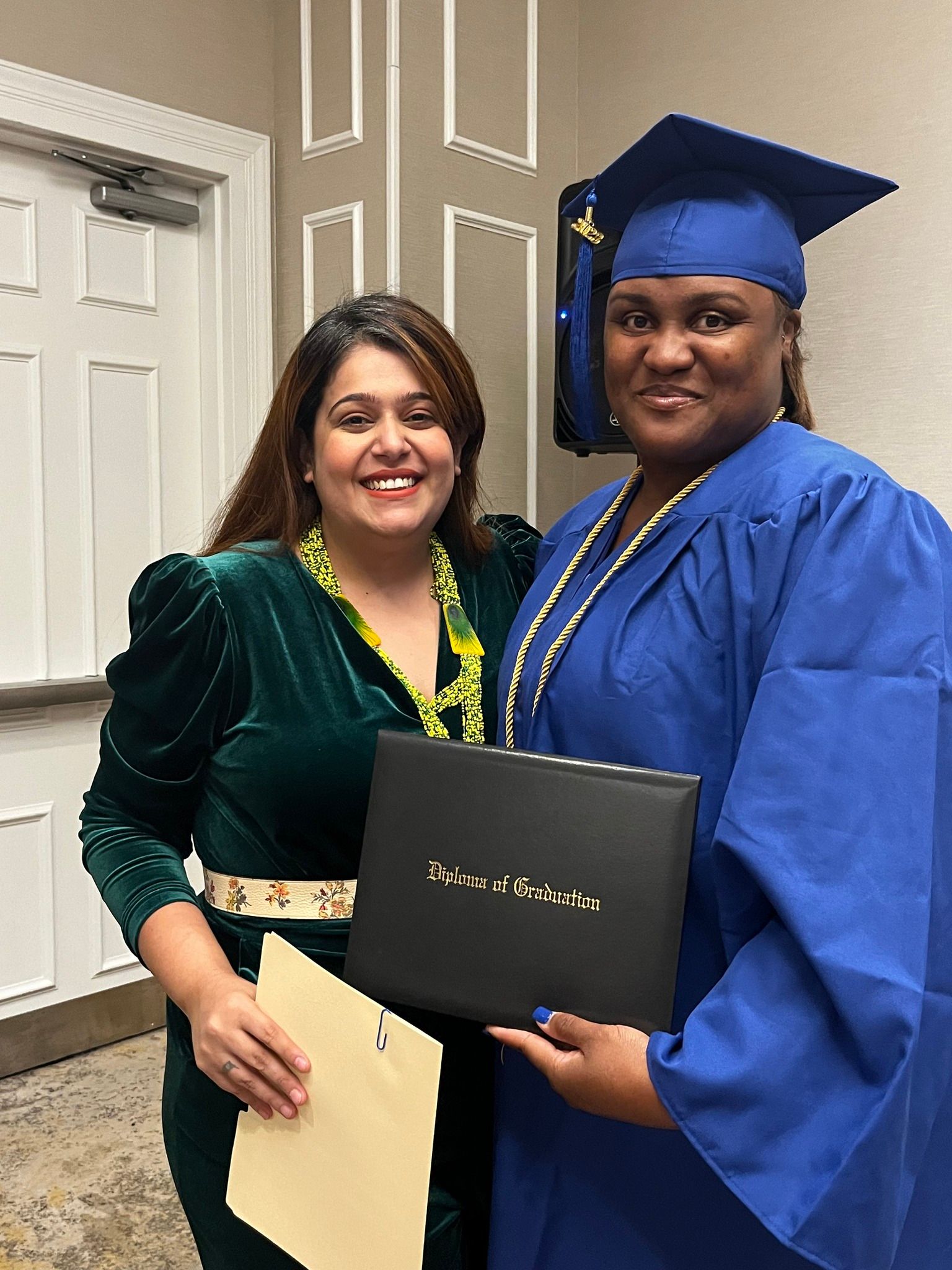 A woman in a graduation cap and gown is standing next to another woman holding a diploma.