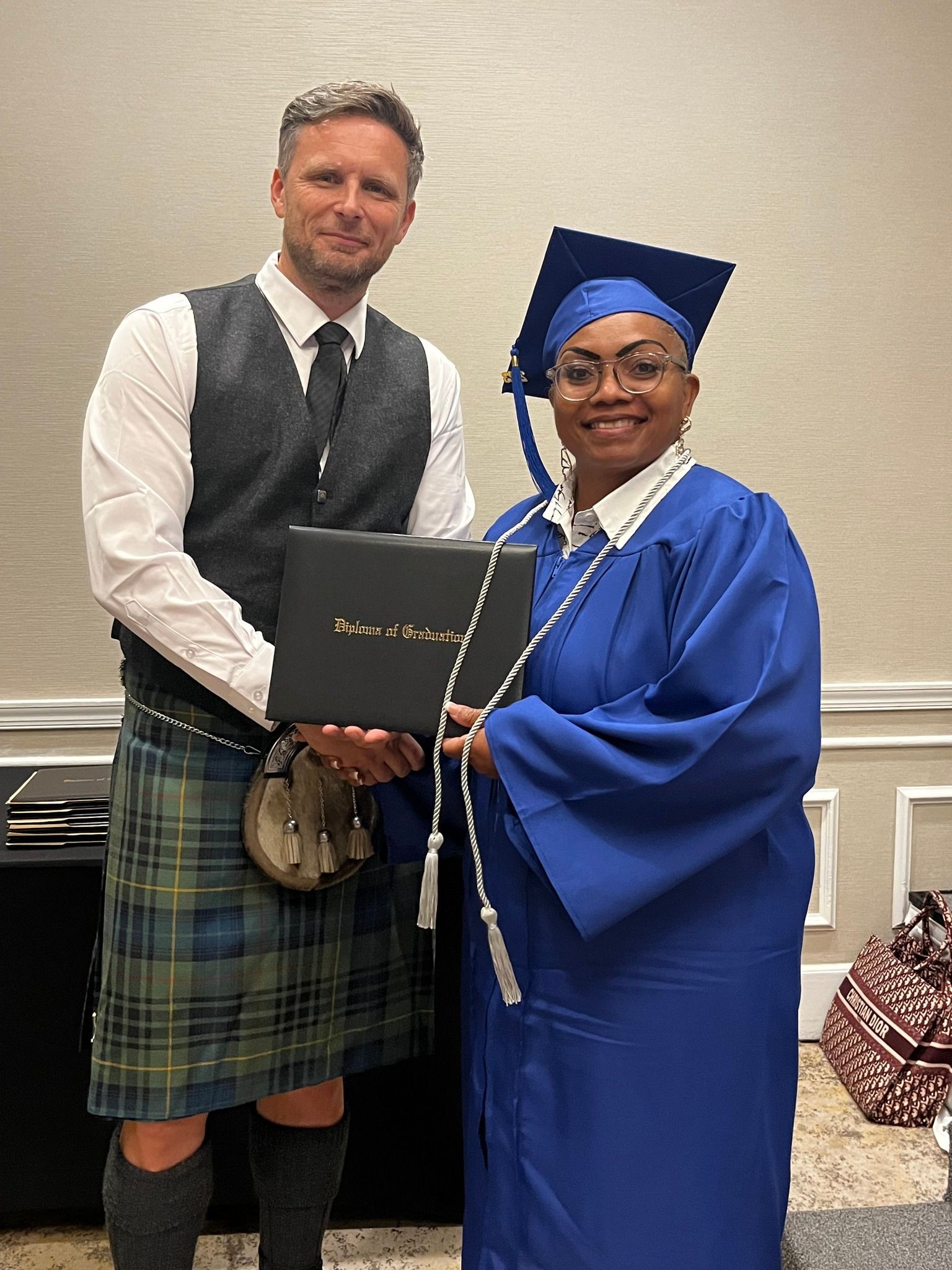 A man in a kilt is shaking hands with a woman in a graduation cap and gown.