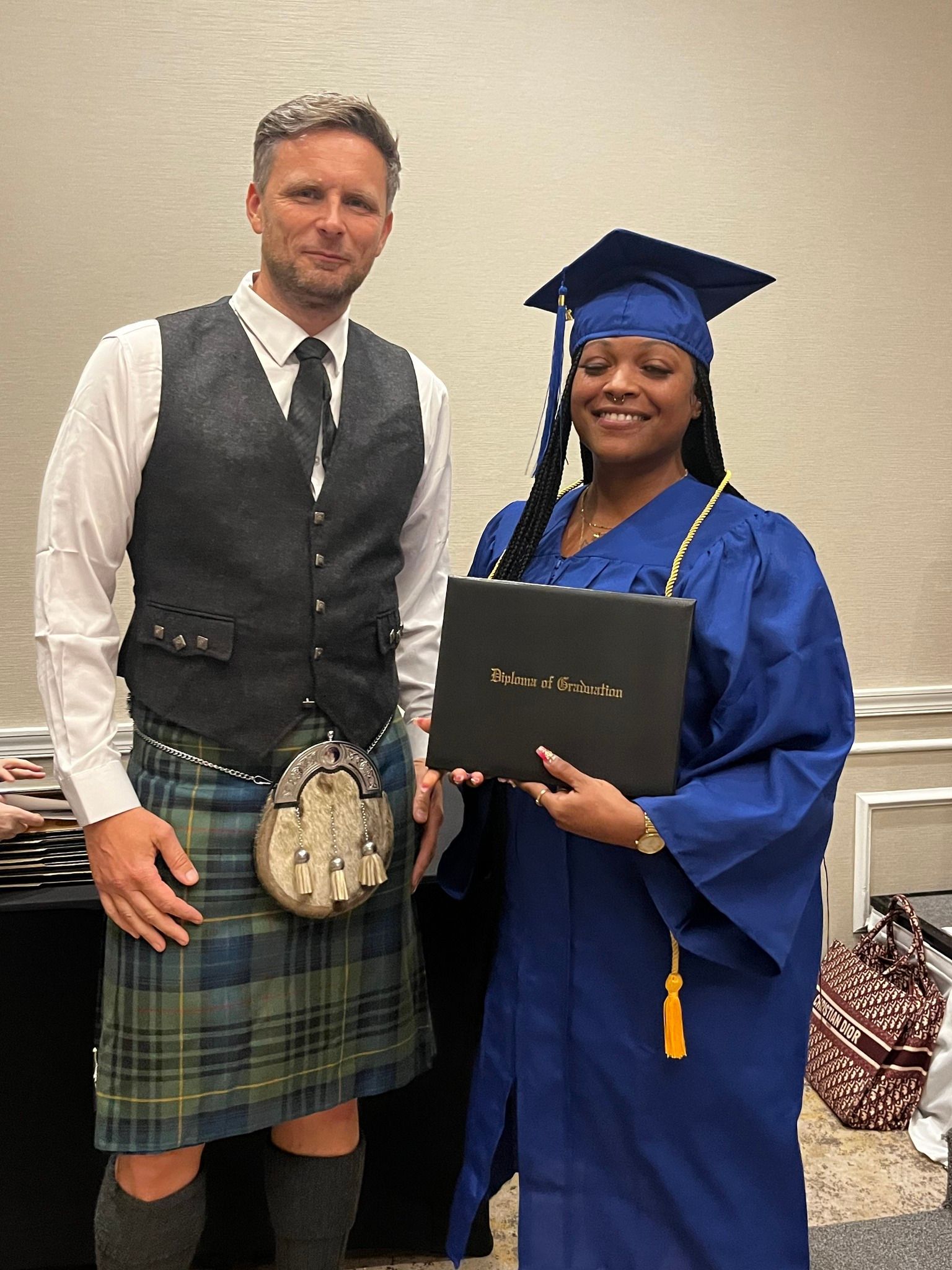 A man in a kilt is standing next to a woman in a graduation cap and gown holding a diploma.