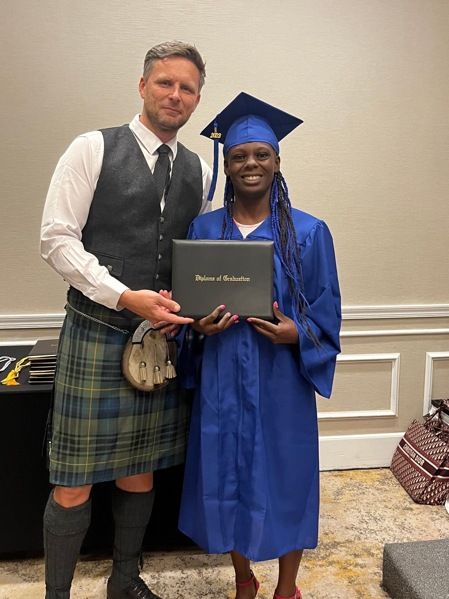 A man in a kilt is standing next to a woman in a graduation cap and gown holding a diploma.