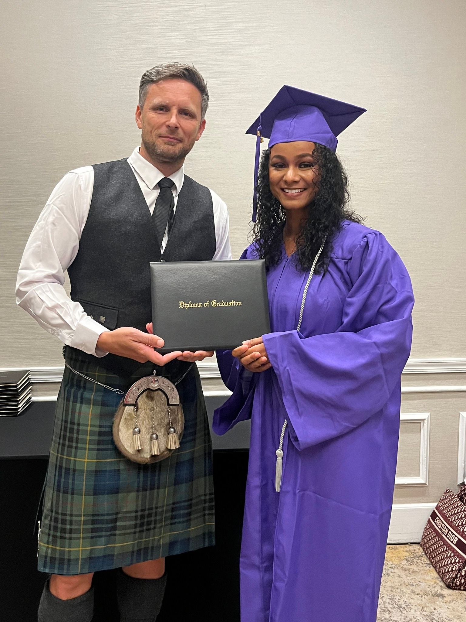 A man in a kilt is holding a diploma next to a woman in a purple gown.