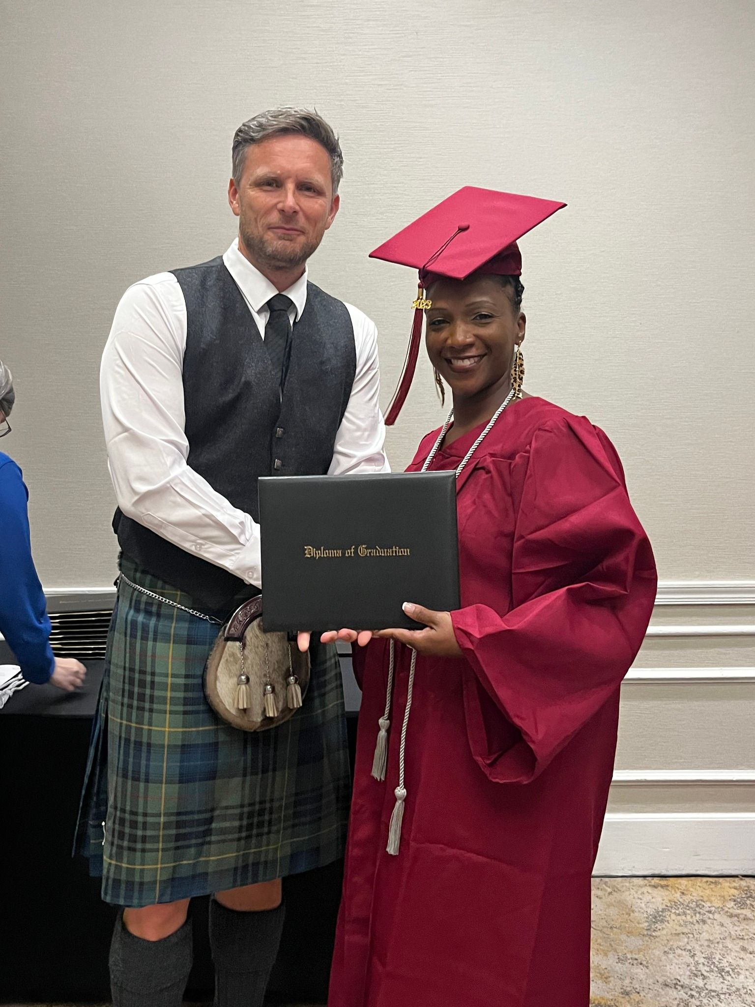 A man in a kilt is standing next to a woman in a graduation cap and gown holding a diploma.