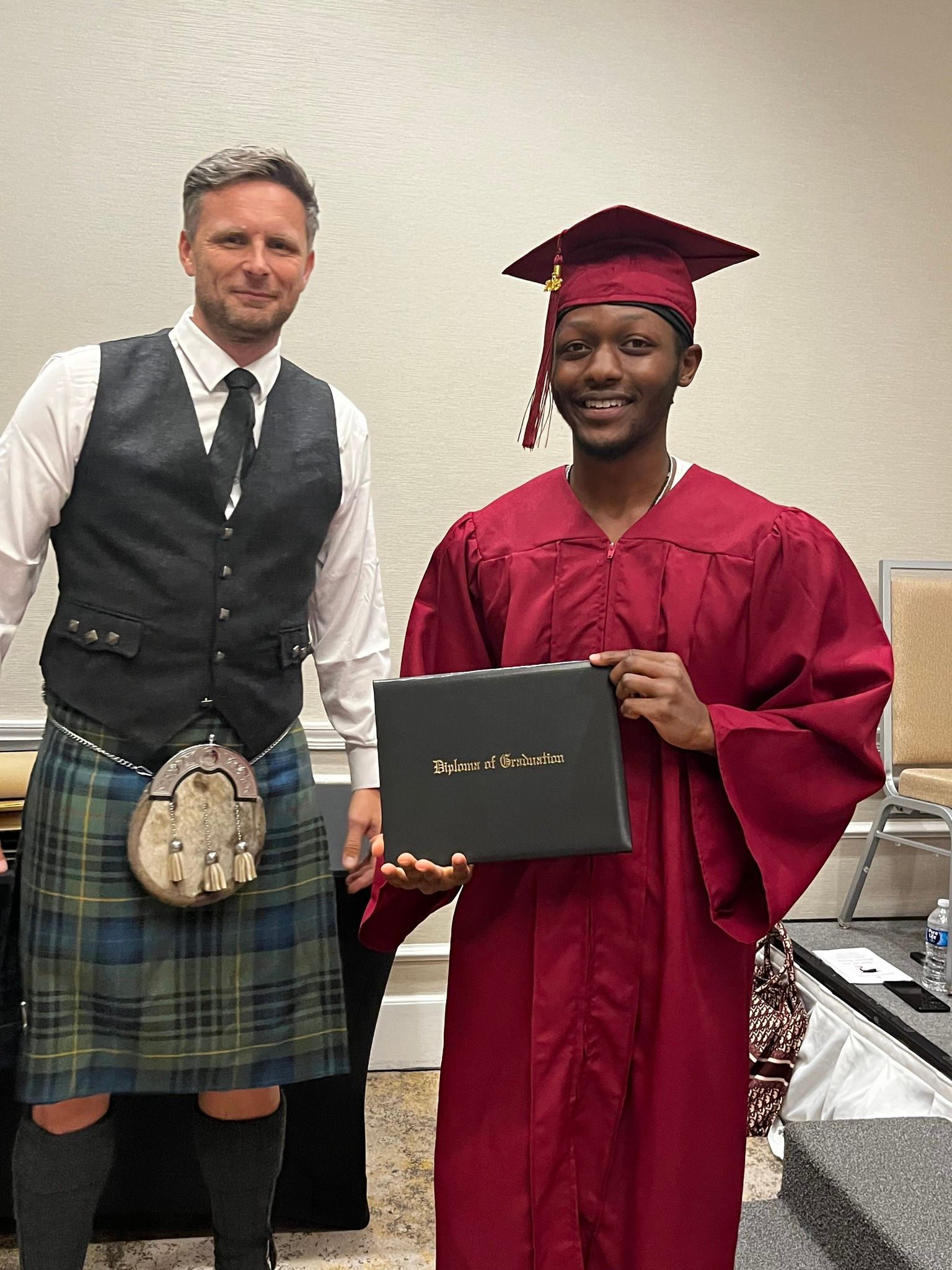 A man in a kilt is standing next to a man in a graduation cap and gown holding a diploma.