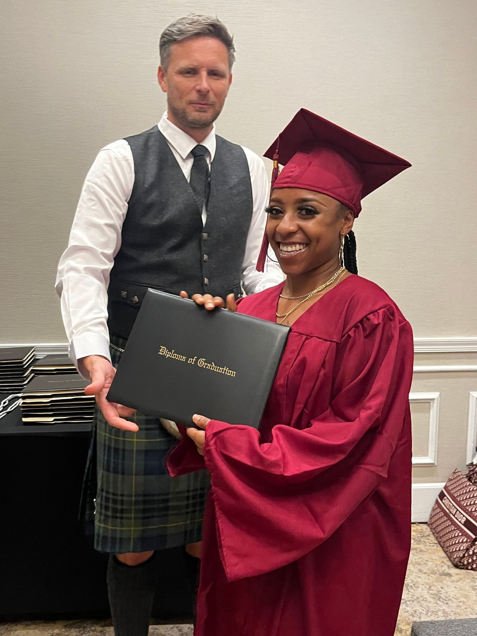A man in a kilt is standing next to a woman in a graduation cap and gown holding a diploma.