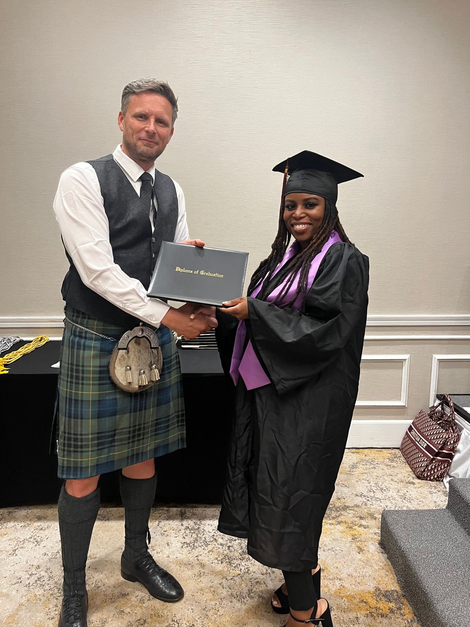 A man in a kilt is shaking hands with a woman in a graduation cap and gown.