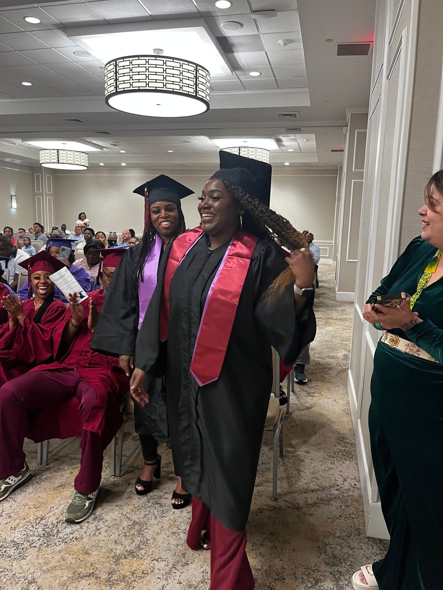 A woman in a graduation cap and gown is standing in front of a crowd of people.
