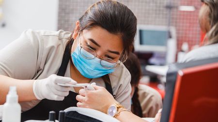 A woman is wearing a mask and gloves while getting her nails done.