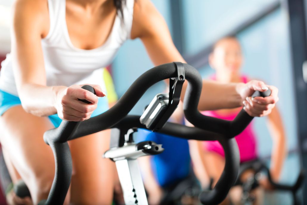 Person exercising on a stationary bike in a gym class, gripping black handlebars.