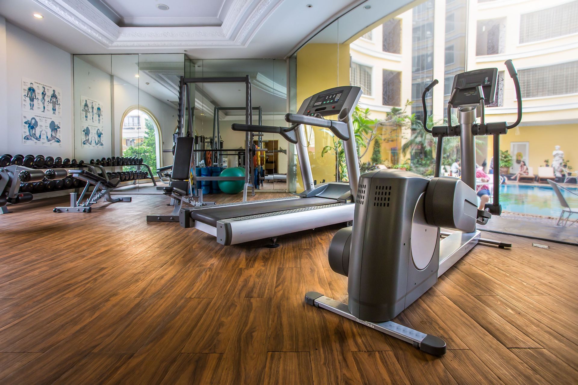 Modern gym with treadmills, exercise bikes, dumbbells, and large windows overlooking a building courtyard