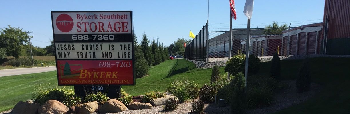 Sign for Bykerk Southfield Storage with phone numbers, next to a road and grassy area.