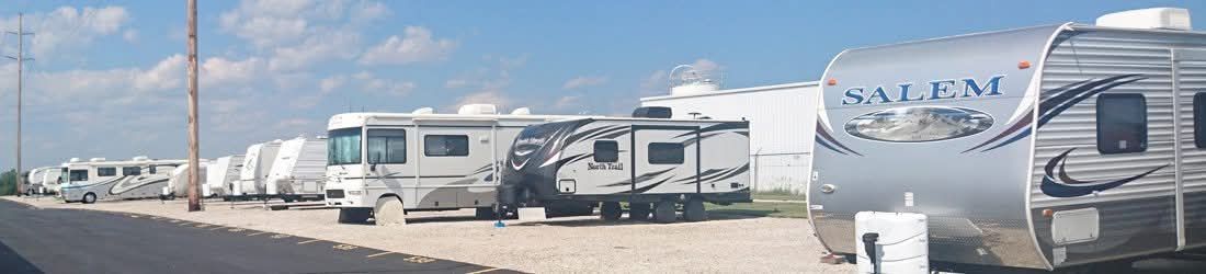 RVs parked on a gravel lot under a blue sky, with some utility poles in the background.