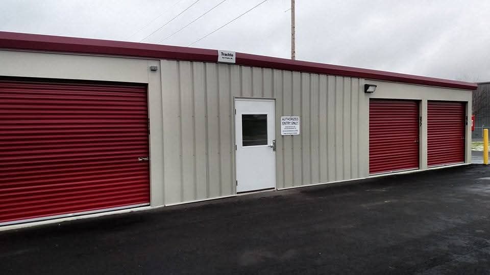 Storage units with red doors, white door, beige walls, and asphalt driveway.
