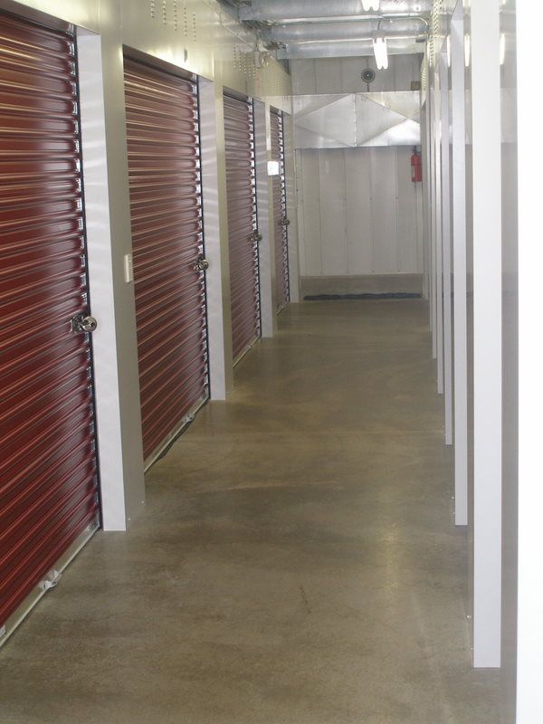 Storage unit corridor with red doors and concrete floor.