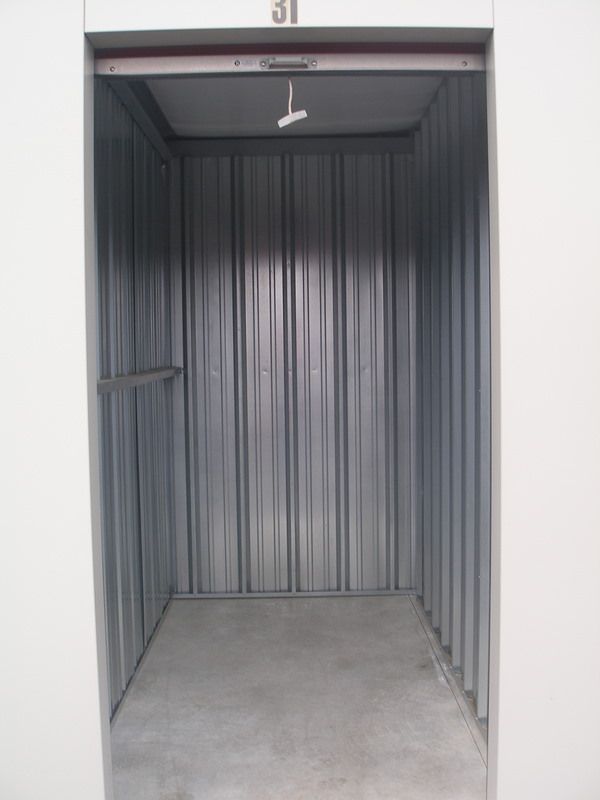 Empty storage unit with gray corrugated metal walls and concrete floor.