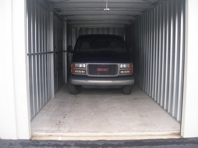 A dark blue GMC van parked inside a metal storage unit with a concrete floor.