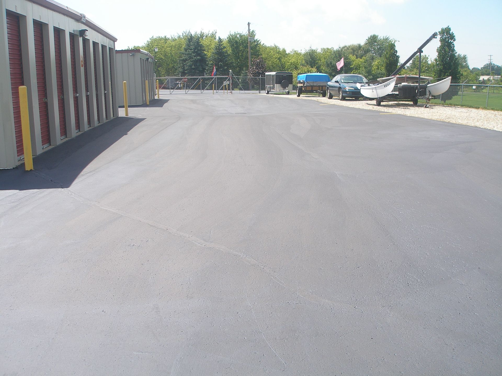 Asphalt driveway leading past storage units and parked vehicles on a sunny day.